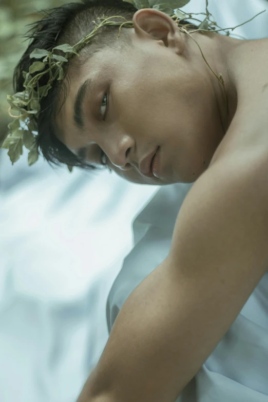 a man laying in bed with a flower crown on his head, by Shen Quan, pexels contest winner, renaissance, portrait of teenage aphrodite, soft morning lighting, male with halo, film still