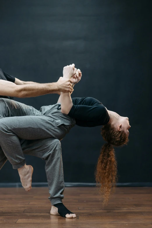 a man and woman doing a handstand on a wooden floor, by Elizabeth Polunin, arabesque, on a gray background, woman holding another woman, sydney hanson, university