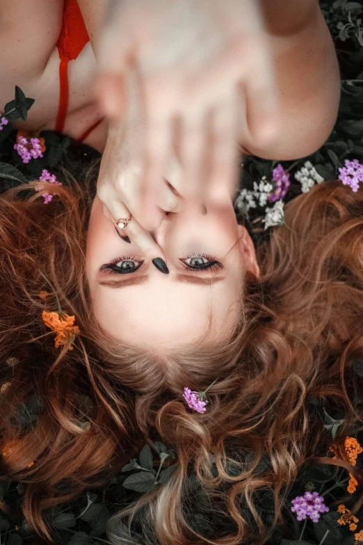 a woman laying on top of a lush green field of flowers, trending on pexels, aestheticism, brown-red-hair pretty face, slit pupils, show from below, high angle