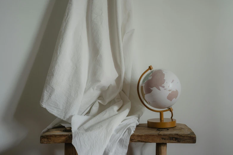 a globe sitting on top of a wooden table, a marble sculpture, by Jessie Algie, white sheets, studio shoot, linen, coloured