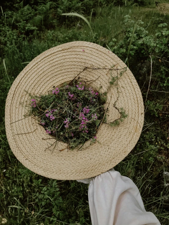 a person holding a straw hat with flowers in it, by Anna Boch, unsplash, land art, covered in vines, low quality photo, ignant, lobelia