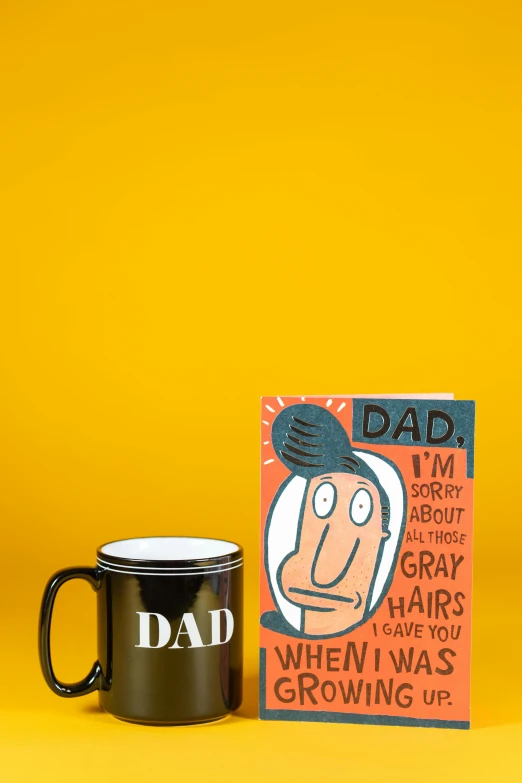 a mug and card on a yellow background, a cartoon, by Paul Bird, dada, with dark grey hair, dad, & a dark, f/2