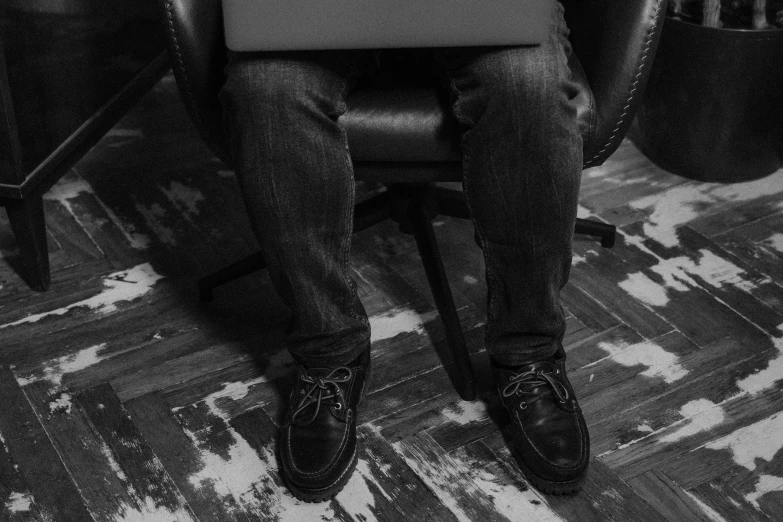 a person sitting in a chair with a laptop, a black and white photo, by Romain brook, pexels, jeans and black boots, texturized, corporate boss, grunge