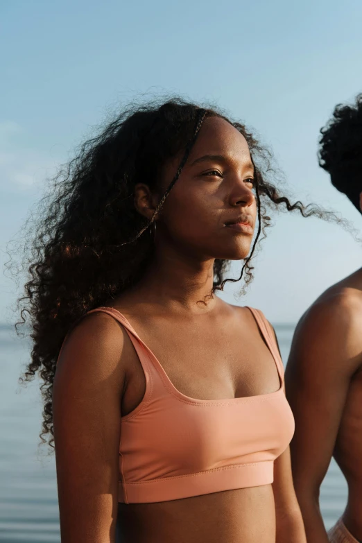 a man and a woman standing next to each other on a beach, trending on unsplash, renaissance, light skinned african young girl, cute girl wearing tank suit, focused on her neck, curls on top