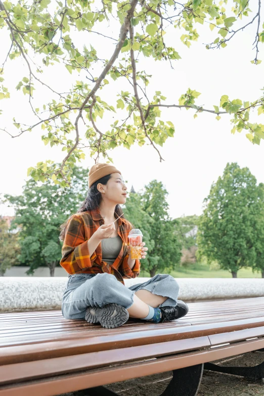 a woman sitting on top of a wooden bench, by Jang Seung-eop, trending on pexels, drinking a strawberry iced latte, sitting under a tree, corn, wearing casual clothing