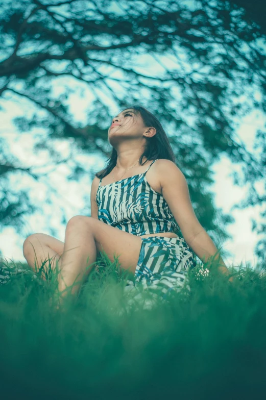 a woman sitting on top of a lush green field, inspired by Elsa Bleda, pexels contest winner, patterned clothing, low-angle, attractive girl, blue mood