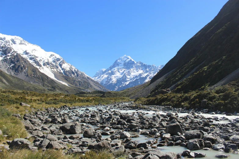 a river running through a lush green valley, by James Ardern Grant, unsplash, hurufiyya, with a snowy mountain and ice, avatar image, clear blue skies, gravel and scree ground