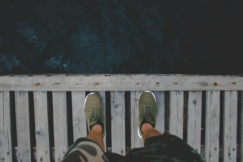 a person standing on a bridge next to a body of water, pexels contest winner, acid-green sneakers, wearing cargo pants, sitting on a mocha-colored table, looking down at you