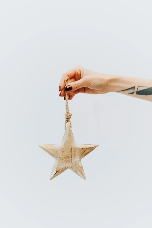 a person holding a wooden star ornament, a tattoo, trending on pexels, folk art, plain background, - 9, hanging, light tan