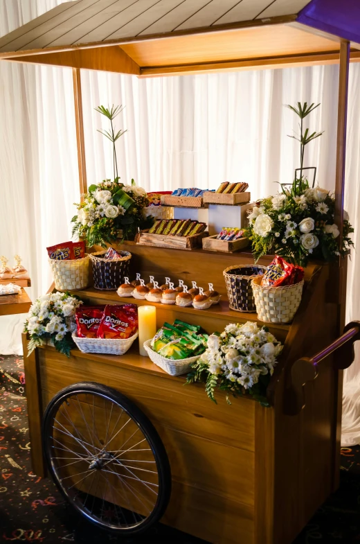 a wooden cart filled with lots of food, desserts, bicycles, indoor setting, bouquet