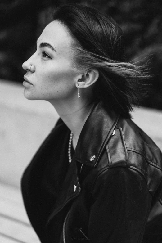 a black and white photo of a woman sitting on a bench, inspired by Louisa Matthíasdóttir, trending on pexels, realism, wearing leather jacket, profile image, kiko mizuhara, strong jawline