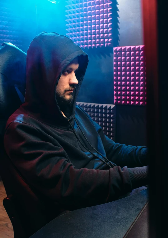 a man in a hoodie sitting in front of a computer, sitting on a throne, profile image, techwear clothes, somber lighting