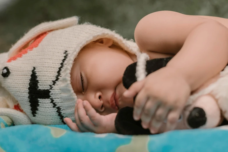 a baby sleeping on a blanket with a stuffed animal, pexels contest winner, symbolism, small hat, avatar image, manuka, teemo from league of legends