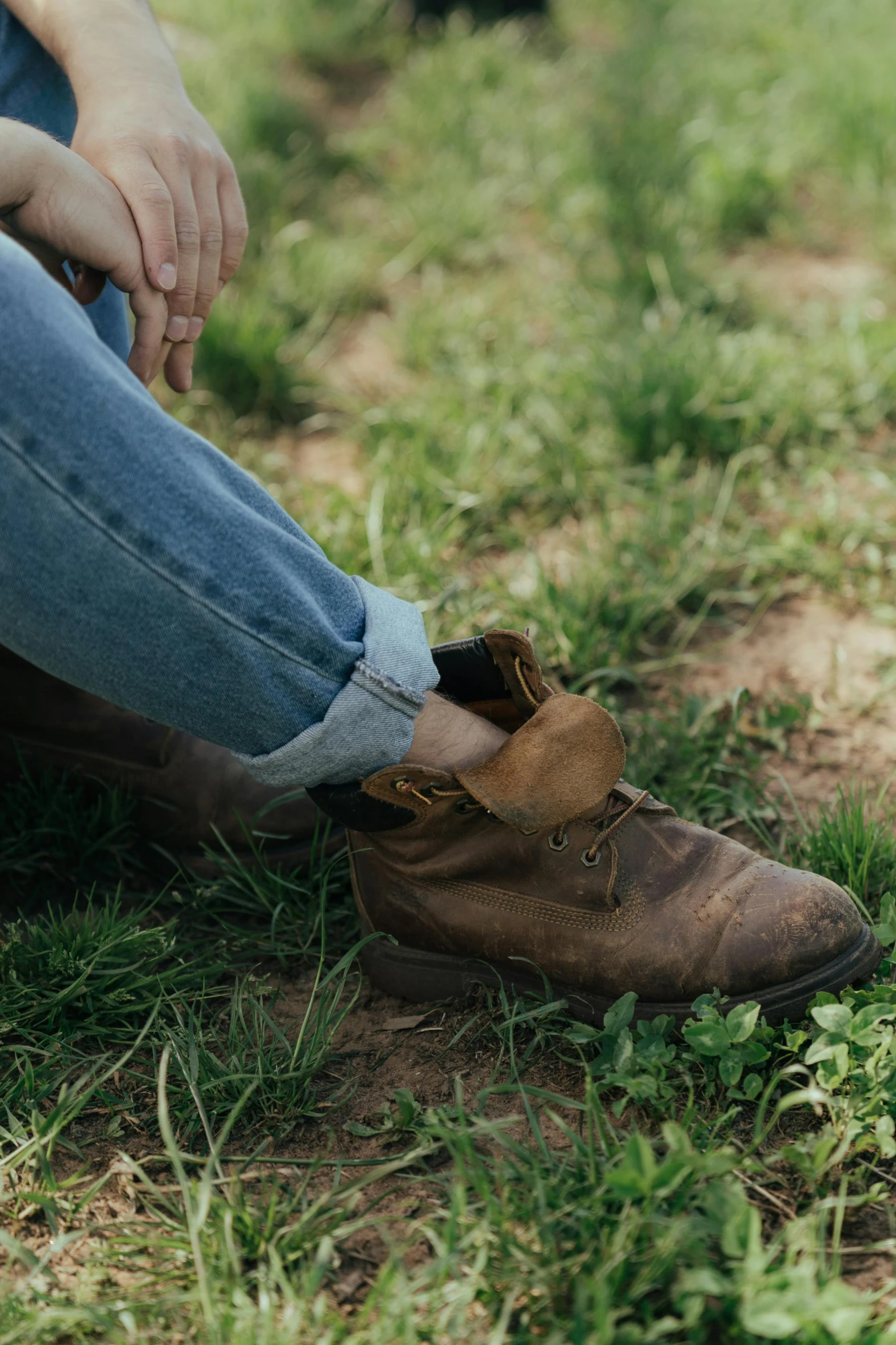 a woman sitting on top of a lush green field, by Jessie Algie, trending on pexels, renaissance, leather shoes, rustic and weathered, jeans, 33mm photo