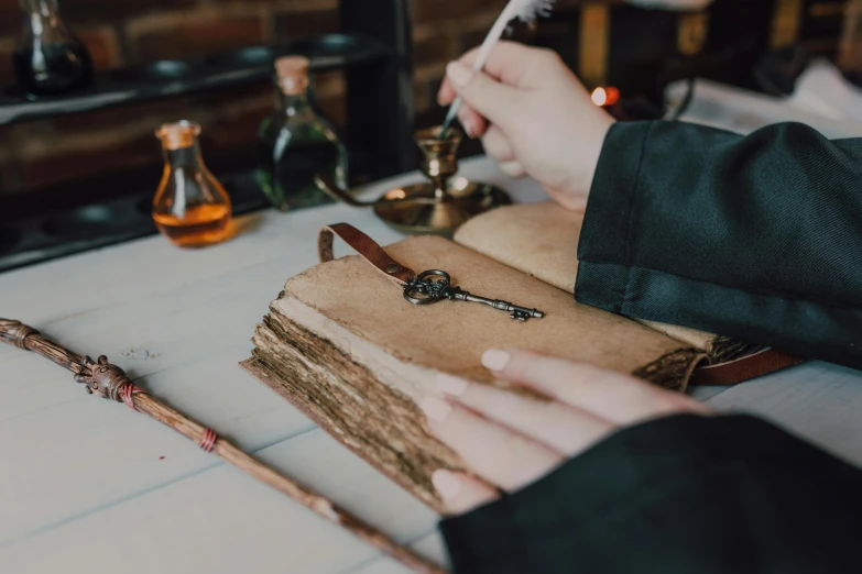 a person sitting at a table writing on a book, an album cover, trending on pexels, arts and crafts movement, steampunk style weapons, apothecary, wooden magic wand, the key of life