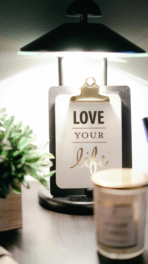 a lamp sitting on top of a desk next to a cup of coffee, a picture, by Robbie Trevino, pexels, style lettering, love theme, jar on a shelf, holding a clipboard