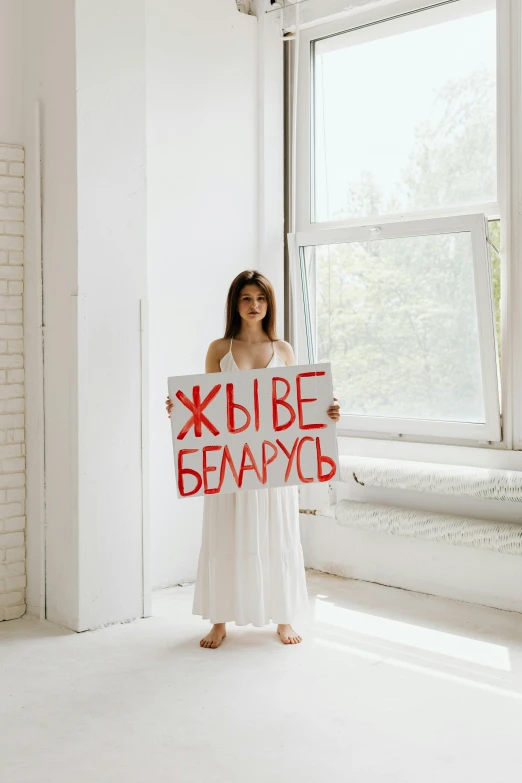 a woman standing in front of a window holding a sign, a poster, by Julia Pishtar, pexels contest winner, feminist art, president of belorussia, in white room, 000 — википедия, young beautiful