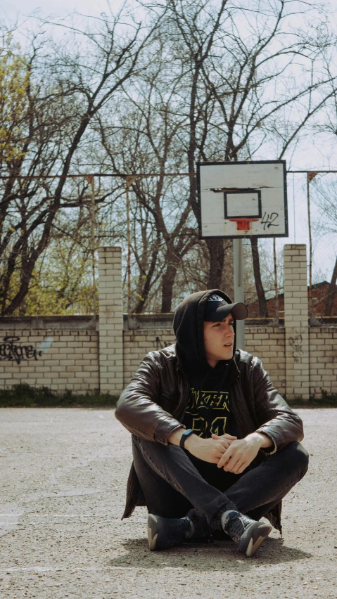 a man sitting on the ground in front of a basketball hoop, an album cover, by Attila Meszlenyi, pexels contest winner, hat and hoodie, 15081959 21121991 01012000 4k, headshot profile picture, instagram picture