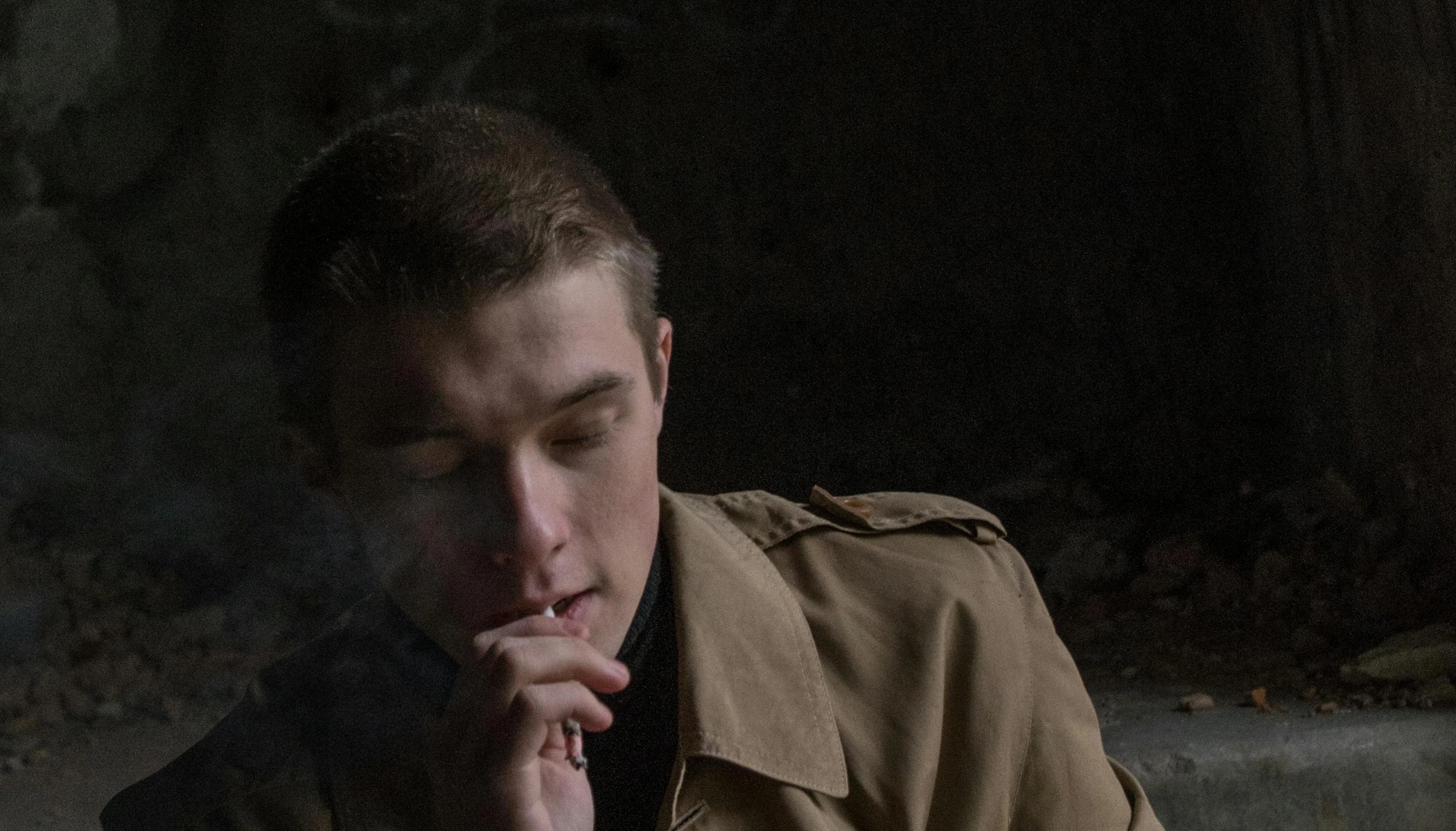 a man in a trench coat smokes a cigarette, a portrait, unsplash, visual art, yung lean, in a cave. underexposed, dean winchester, praying with tobacco