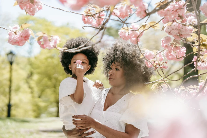 a woman holding a child under a cherry tree, pexels contest winner, curly afro, avatar image, photoshoot for skincare brand, white blossoms