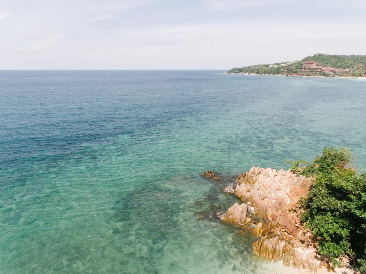 a large body of water next to a lush green hillside, a photo, unsplash, standing on a beach in boracay, cannes, mermaids in distance, manly