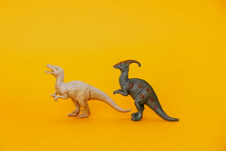 a couple of toy dinosaurs standing next to each other, trending on unsplash, in front of an orange background, upscaled to high resolution, on a pale background, velociraptor