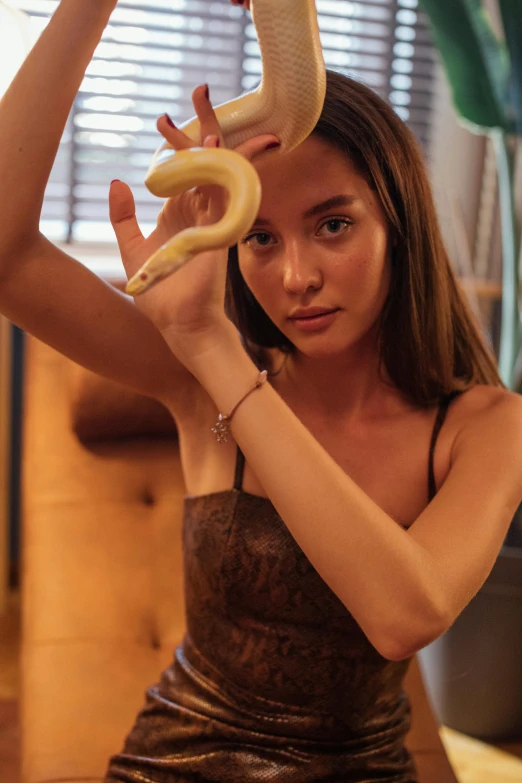 a woman holding a snake over her head, trending on pexels, photorealism, dilraba dilmurat, indoor scene, banana, slightly tanned