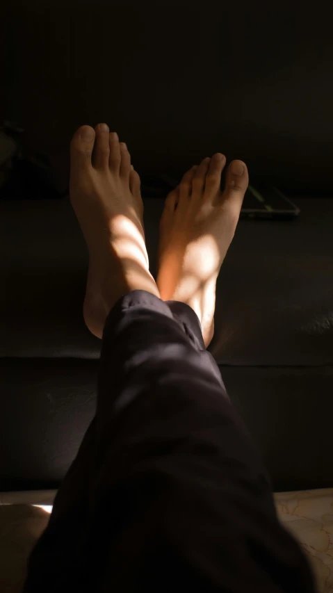 a close up of a person's feet on a couch, light and space, volumetric light from above, high shadow, in a dark studio room, the sun is shining. photographic