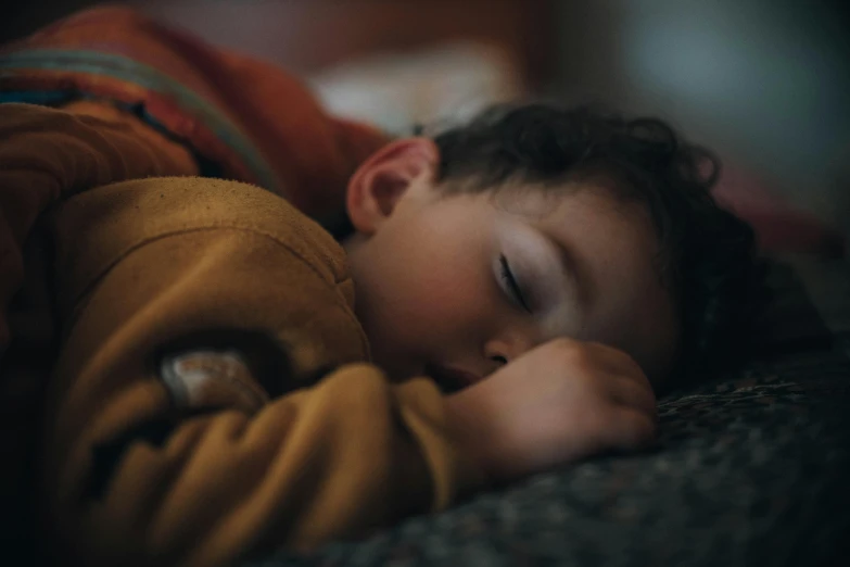 a close up of a child sleeping on a couch, by Matija Jama, pexels contest winner, he is wearing a brown sweater, someone sits in bed, bedhead, animation still