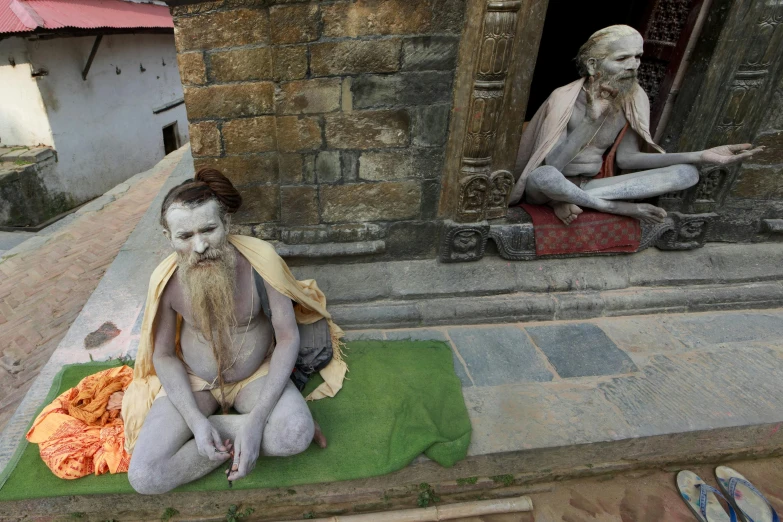 a statue of a man sitting on top of a green mat, two skinny old figures, nepali architecture buildings, photograph credit: ap, die antwoord