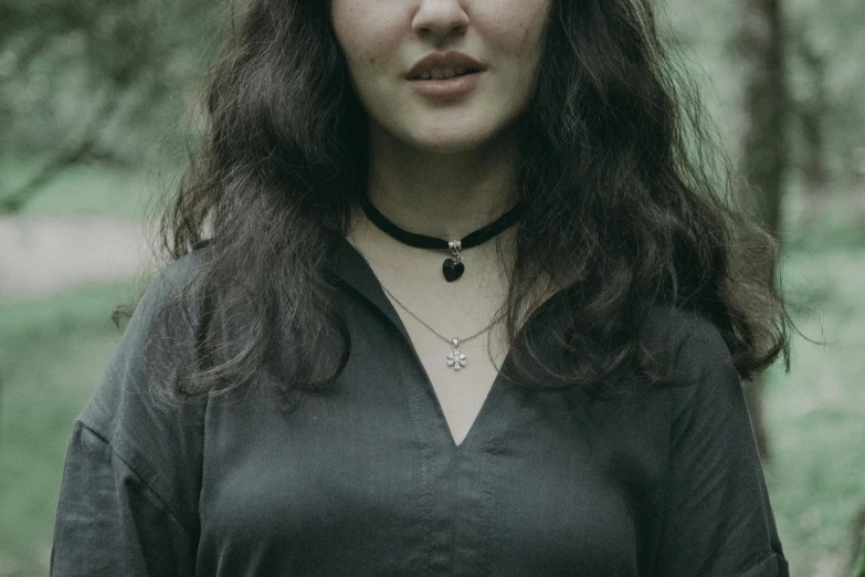 a woman standing in the middle of a forest, a black and white photo, black choker necklace, wearing several pendants, wearing a black shirt, portrait featured on unsplash