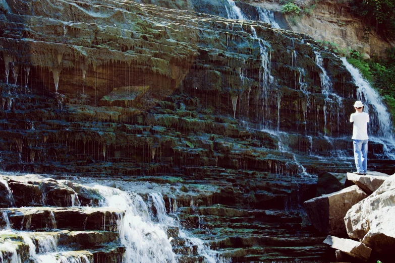 a man standing in front of a waterfall, an album cover, inspired by Elsa Bleda, unsplash, sōsaku hanga, shiny layered geological strata, closeup shot, stephen shore, 1999 photograph