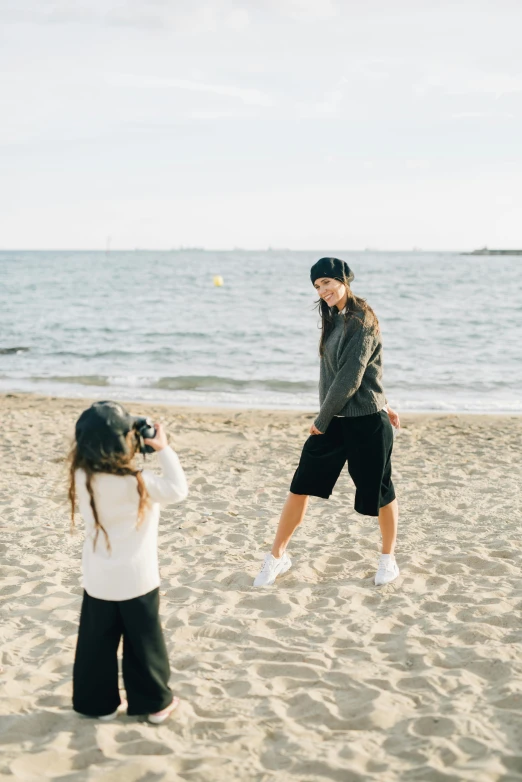 a woman taking a picture of a little girl on the beach, wearing a hoodie and sweatpants, wearing black shorts, 5k, while smiling for a photograph