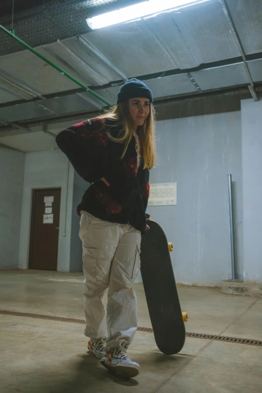 a woman holding a skateboard in a building, a portrait, unsplash, low quality photo, pants, concerned, skate park