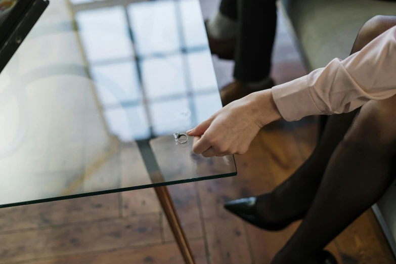 a woman sitting on top of a wooden floor next to a glass table, by Nina Hamnett, pexels contest winner, happening, point finger with ring on it, working in an office, plating, finely detailed furniture