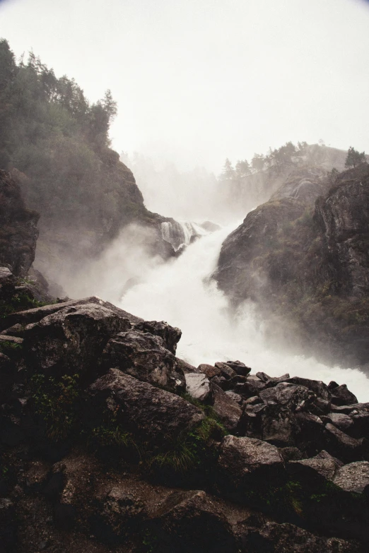 a man standing on top of a rocky cliff next to a waterfall, a picture, inspired by Johan Christian Dahl, pexels contest winner, romanticism, made of mist, 2 5 6 x 2 5 6 pixels, river running through it, norwegian