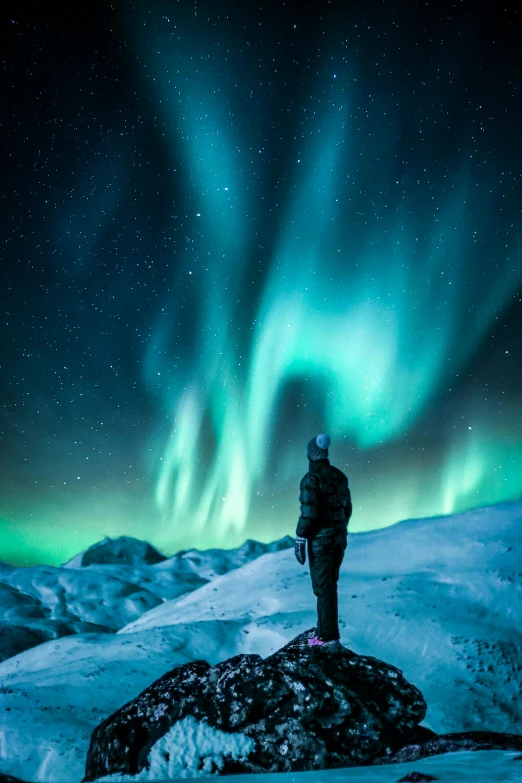 a person standing on top of a snow covered mountain, by Julia Pishtar, pexels contest winner, northen lights background, nat geo, contemplating, colours