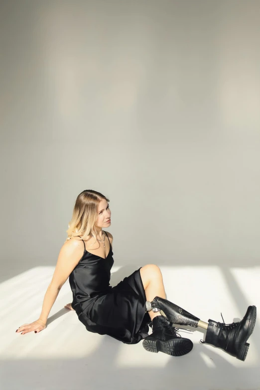 a woman in a black dress sitting on a white surface, wearing a camisole and boots, britt marling style, side light, non binary model