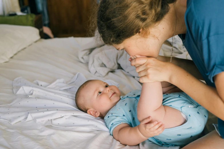 a woman playing with a baby on a bed, pexels contest winner, soft lulling tongue, blue, looking her shoulder, little boy