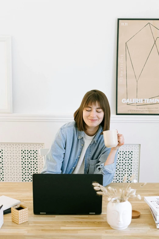 a woman sitting at a table with a laptop and a cup of coffee, curated collections, rebecca sugar, wearing a linen shirt, happy girl