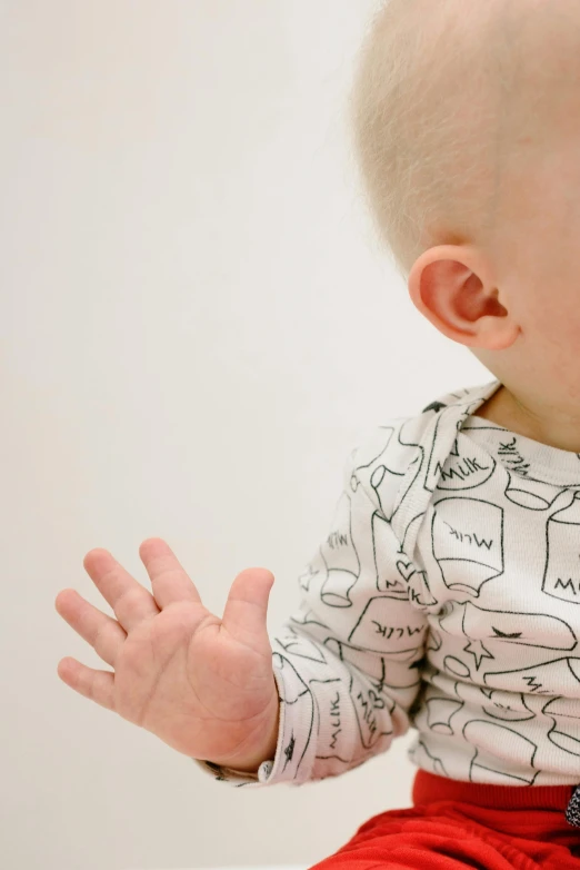 a baby sitting on top of a bed holding a toothbrush, by Nina Hamnett, unsplash, process art, holding his hands up to his face, repeating pattern, printed on a cream linen t-shirt, close up shot from the side