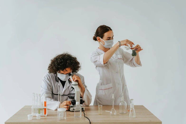 a couple of women standing next to each other at a table, a microscopic photo, by Adam Marczyński, pexels contest winner, spraying liquid, clean white lab background, school class, youtube thumbnail