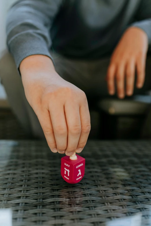 a person playing with a red dice on a table, inspired by Okada Hanko, pink, holding it out to the camera, square, kid named finger