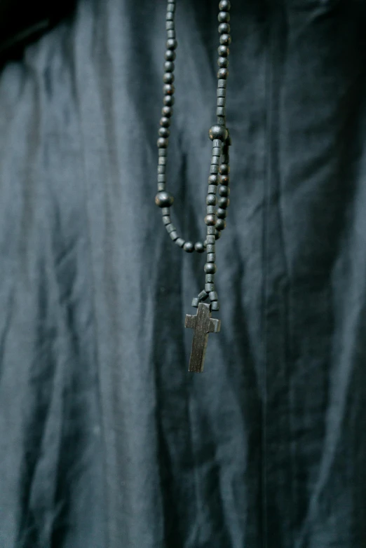 a close up of a person wearing a necklace with a cross on it, unsplash, sōsaku hanga, grey tarnished robes, full - length photo, dark grey, made of bronze