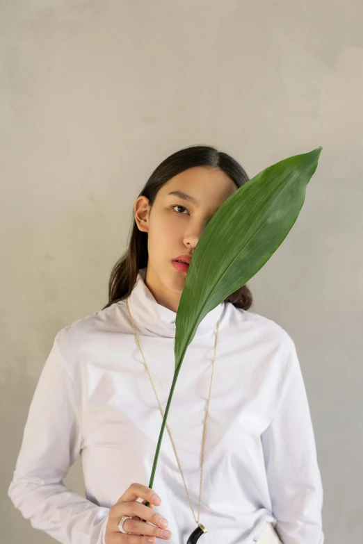 a woman holding a large green leaf in front of her face, an album cover, inspired by Kim Tschang Yeul, minimalism, wearing a white button up shirt, wearing collar on neck, sustainable materials, bella poarch