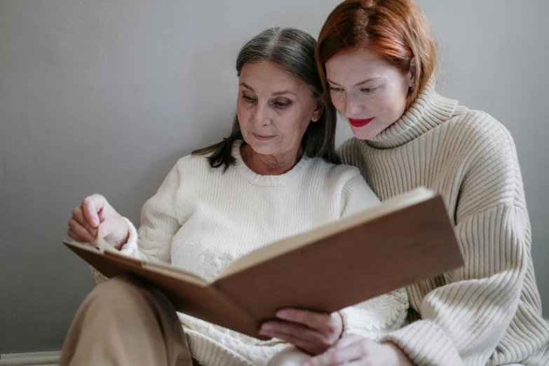 a woman sitting next to a woman reading a book, a photo, trending on pexels, an old lady with red skin, medium head to shoulder shot, grey, thumbnail