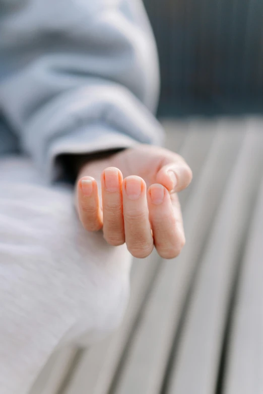 a close up of a person sitting on a bench, long fingers, holding it out to the camera, pale smooth, no text