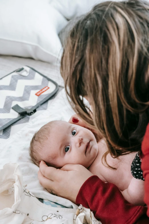 a woman laying on a bed holding a baby, pexels contest winner, happening, first aid kit, grey, seraphine, in detail