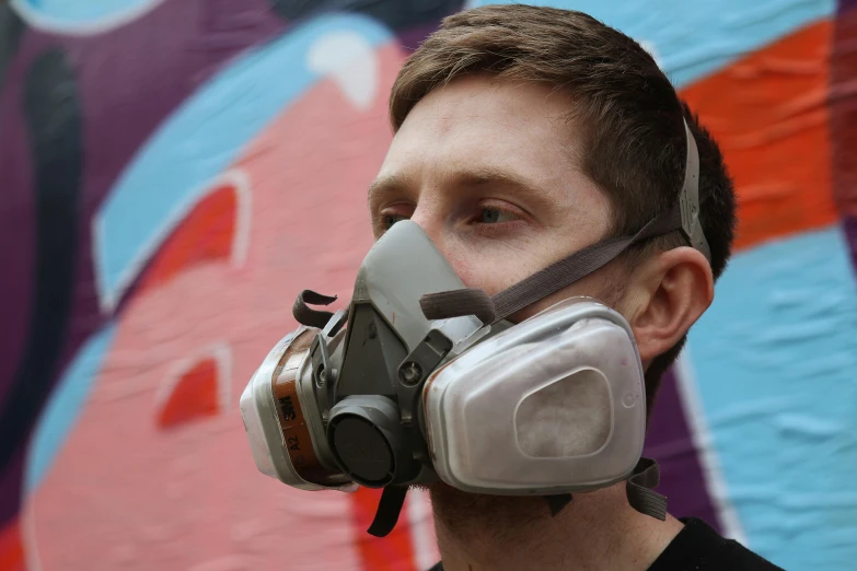 a man wearing a gas mask in front of a graffiti wall, a hyperrealistic painting, by Thomas Furlong, reddit, graffiti, worksafe. instagram photo, close up half body shot, diy, dust mask