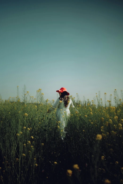 a person in a field with a red hat, inspired by Elsa Bleda, unsplash contest winner, color field, with yellow flowers around it, soft shade, cinematic shot ar 9:16 -n 6 -g, low quality photo